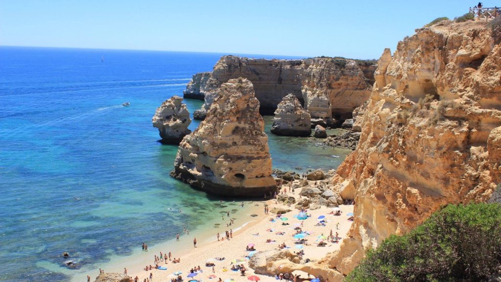 Praia da Marinha, with people on the beach and rock formations protruding from the sea. 
