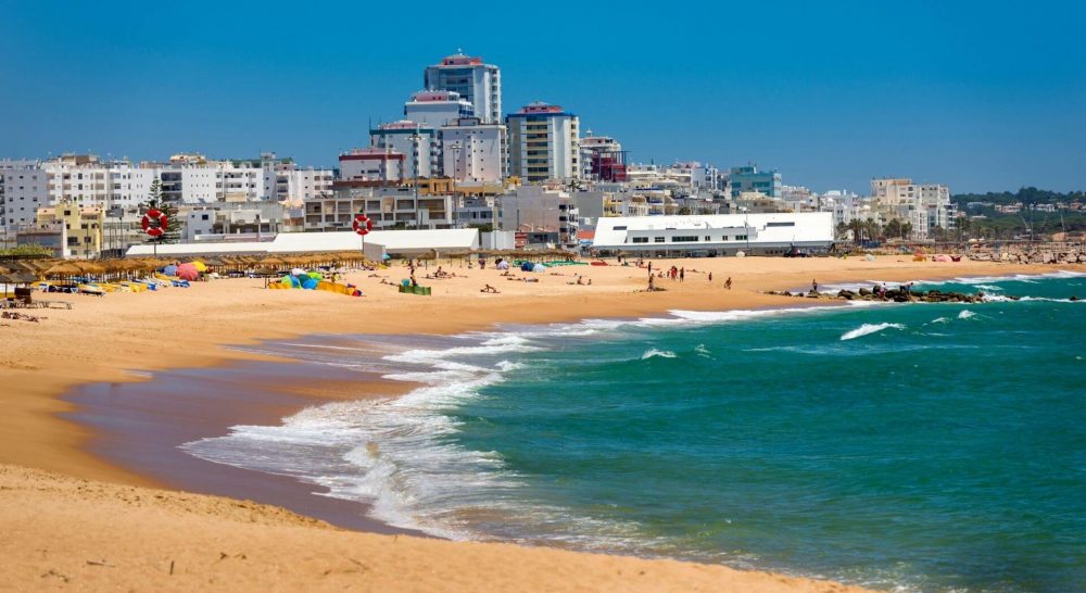 Vilamoura beach with people on the beach and waves breaking on the sand.