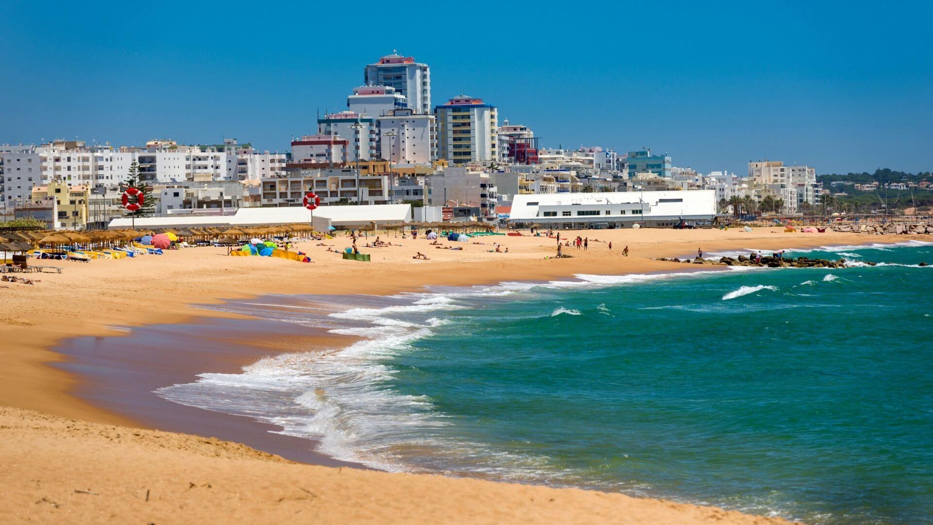 Vilamoura beach with people on the beach and waves breaking on the sand.