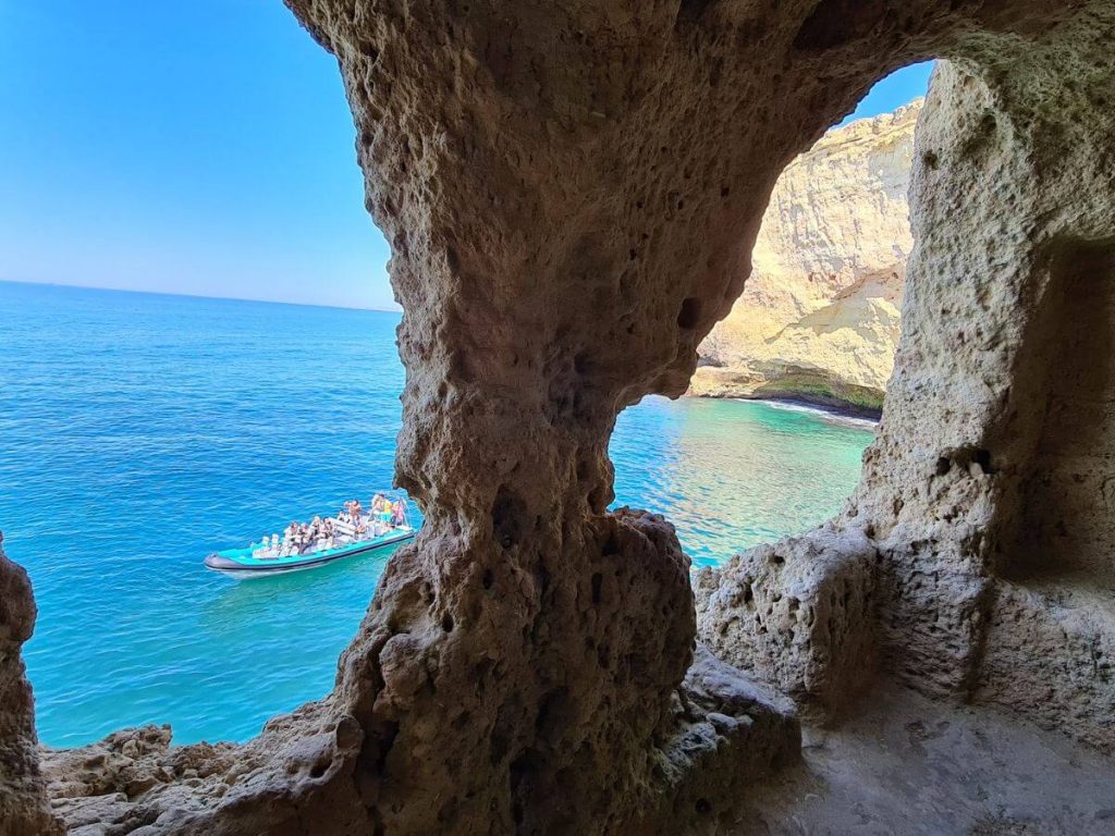 A view from holes in the Algar Seco rock formation overlooking the Atlantic Ocean, with a boat in the sea.
